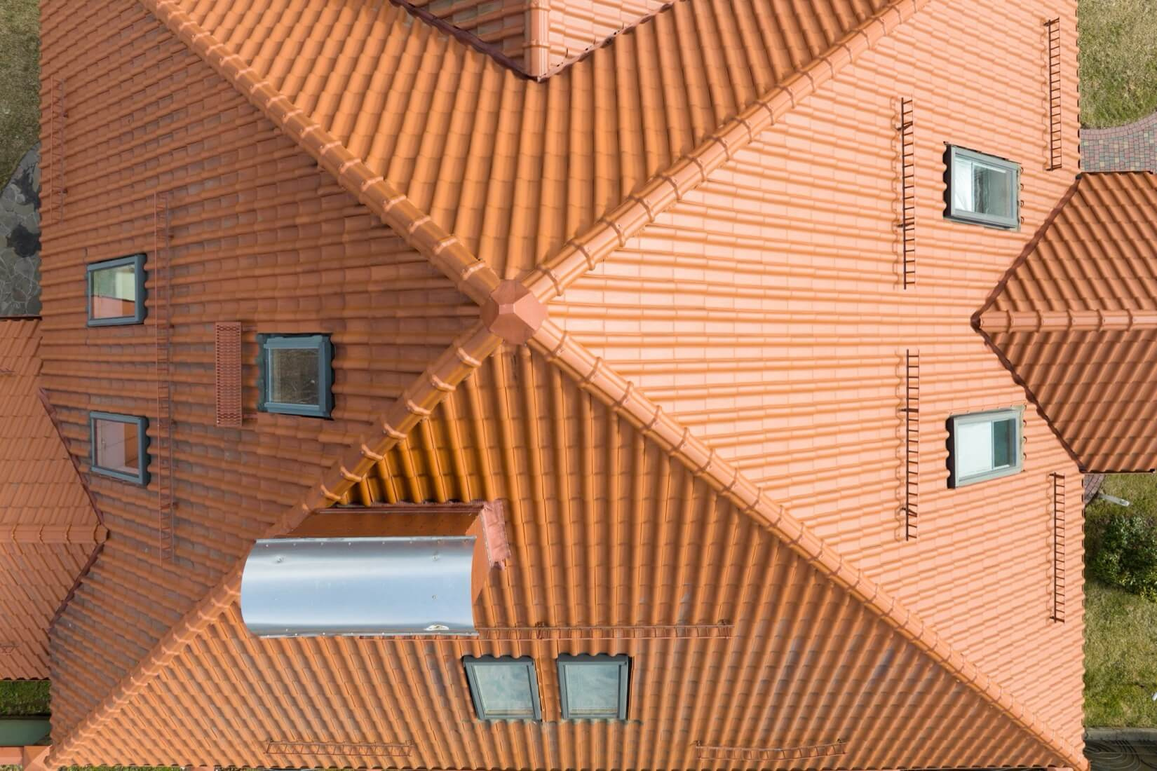 En drönarbild rakt ovanifrån som visar ett stort och komplext tegeltak, vilket framhäver precisionen i en professionell takläggning.