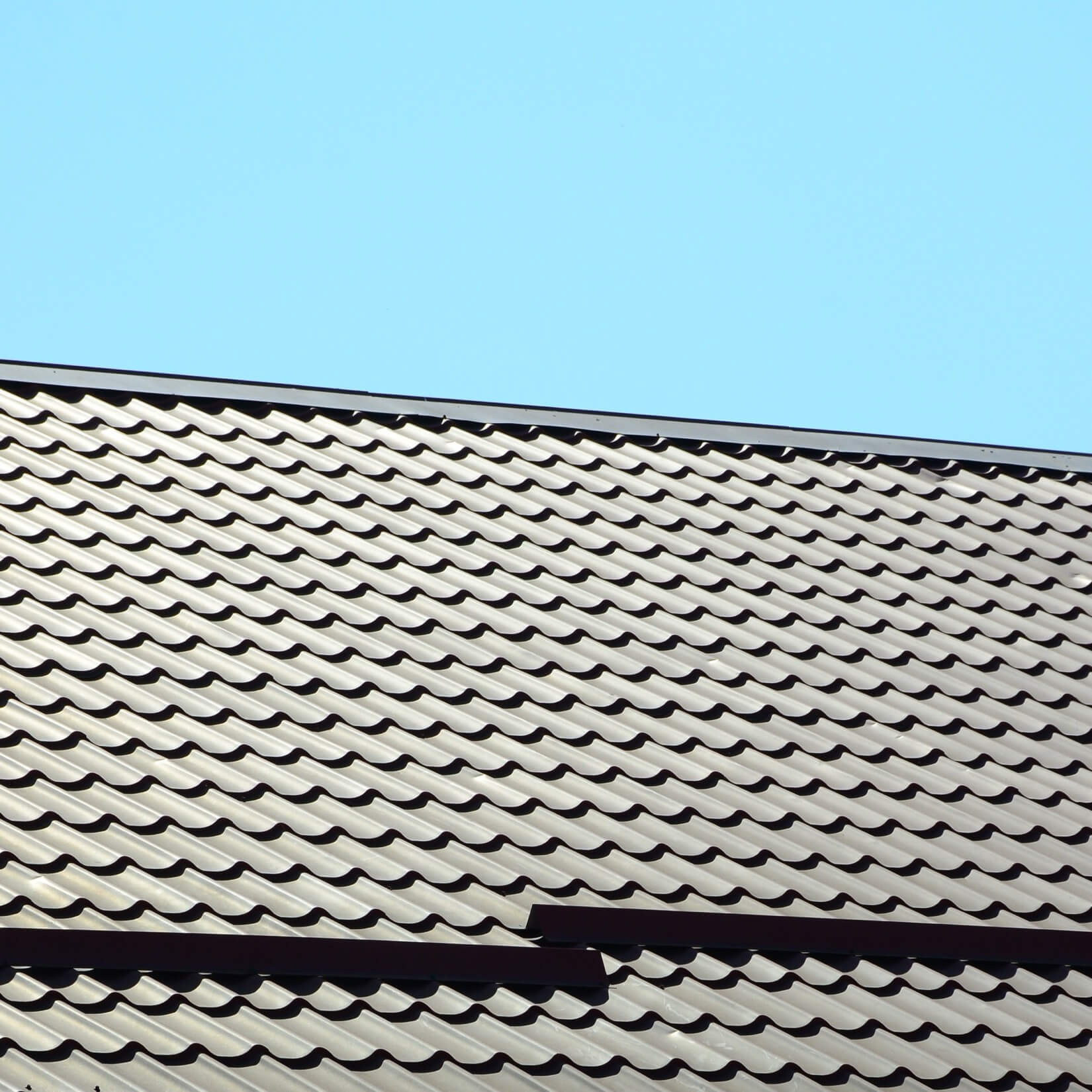 Ett mörkt, vågformat plåttak mot en klarblå himmel, ett populärt och underhållsfritt alternativ vid takläggning.