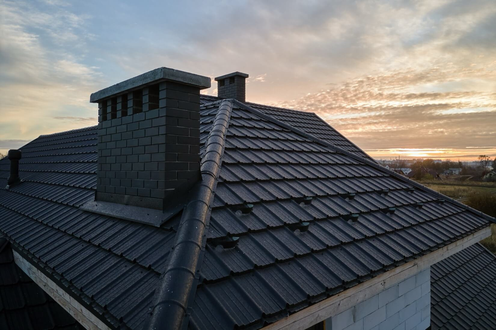 Ett hus med ett nylagt mörkt tak och två skorstenar i solnedgången, som visar slutresultatet av en professionell takläggning.